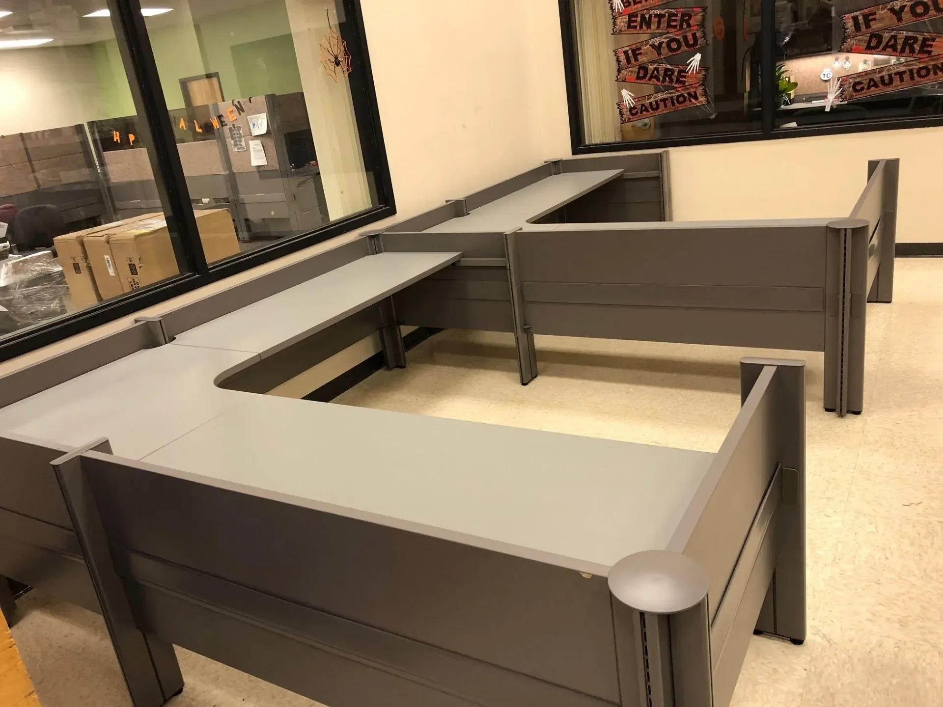 Empty gray cubicles in a modern office room with glass windows and tan flooring