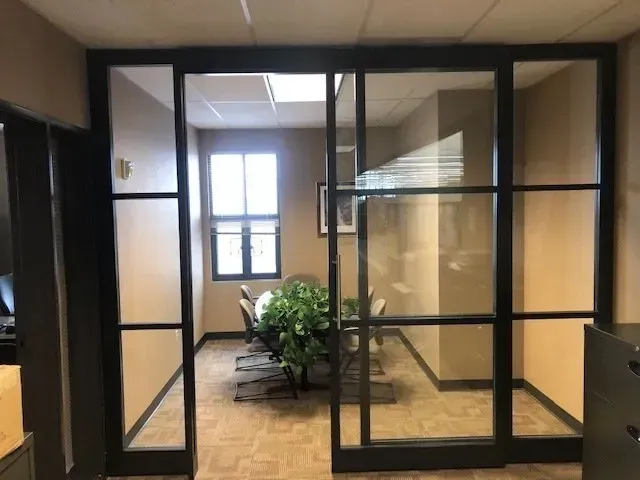 Glass-walled office hallway with a potted plant and window at the far end