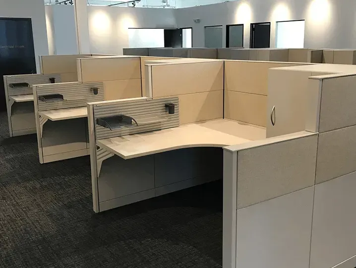 Cubicle office with beige desks, partitions, and shelves in an empty workspace