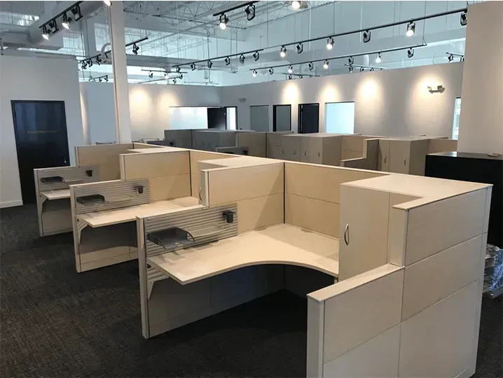 Empty office cubicles in a modern workspace showroom, with beige partitions and dark carpet.