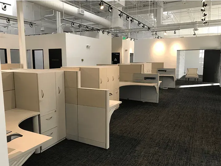 Empty office with beige cubicles, dark carpet, and overhead lighting