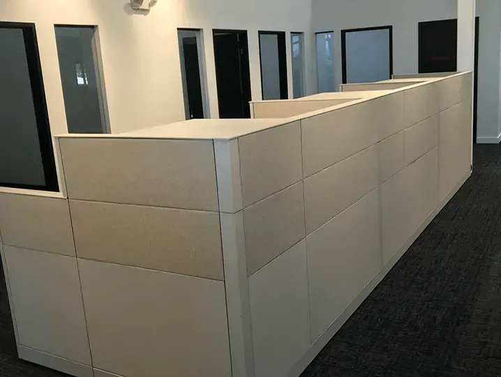 Office hallway with beige cubicle partitions and dark carpet flooring