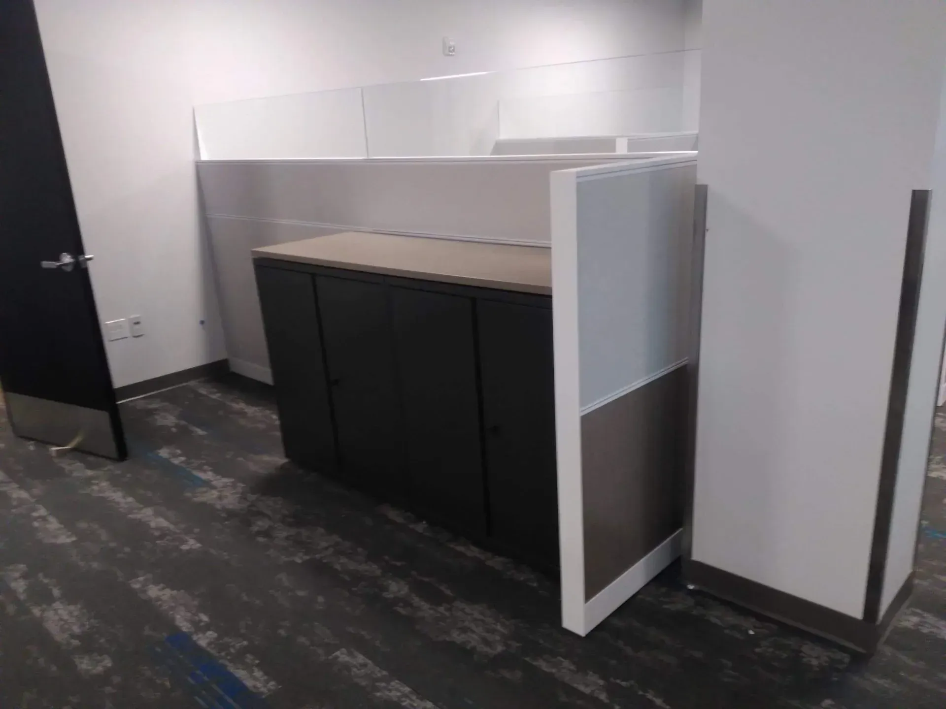 Empty office kitchenette with dark cabinets and white partitions in a gray-floored room