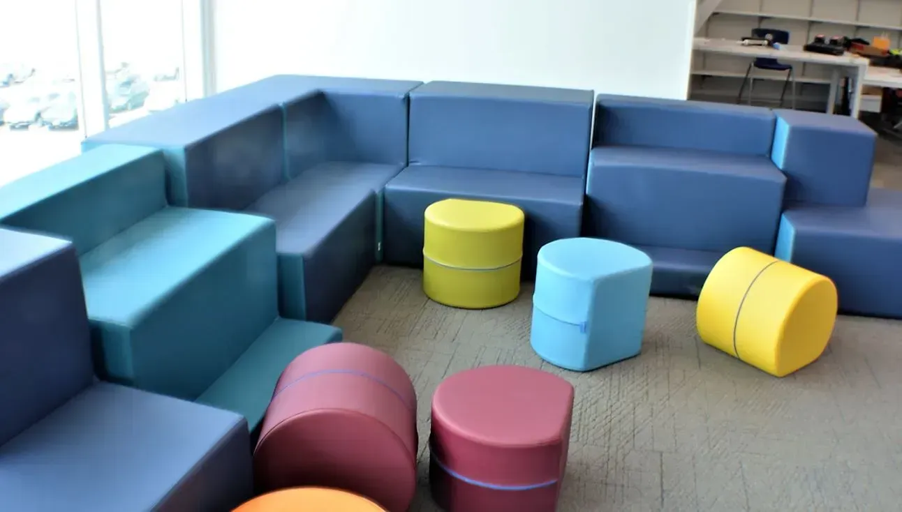 Colorful modular seating in a bright lounge, with blue sofas and round ottomans in yellow, pink, and light blue.