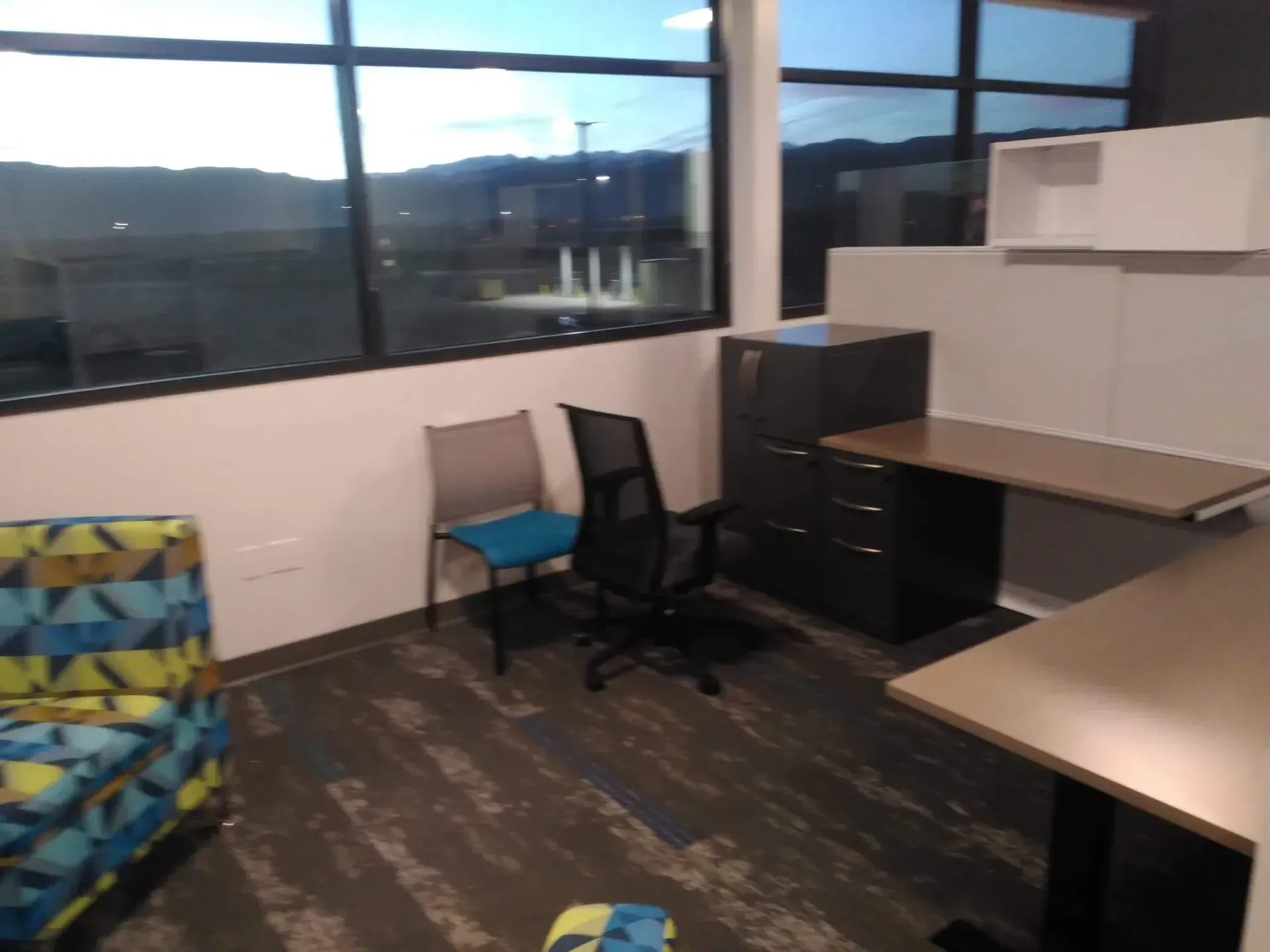 Empty office with desks, chairs, filing cabinet, and large windows overlooking mountains.