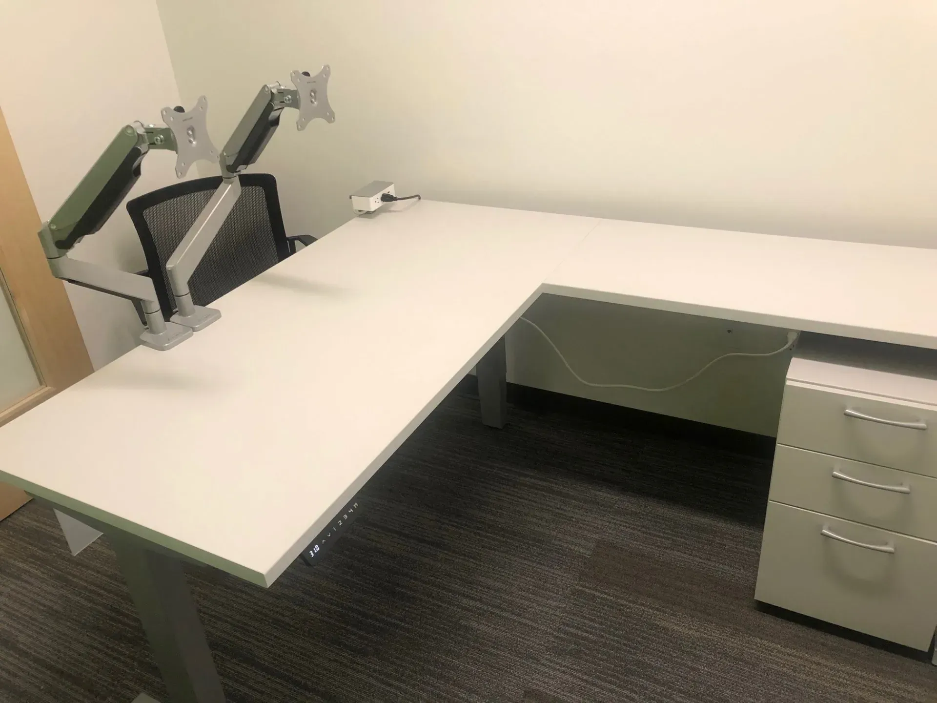 L-shaped white office desk with gray drawers and a chair in a small office room