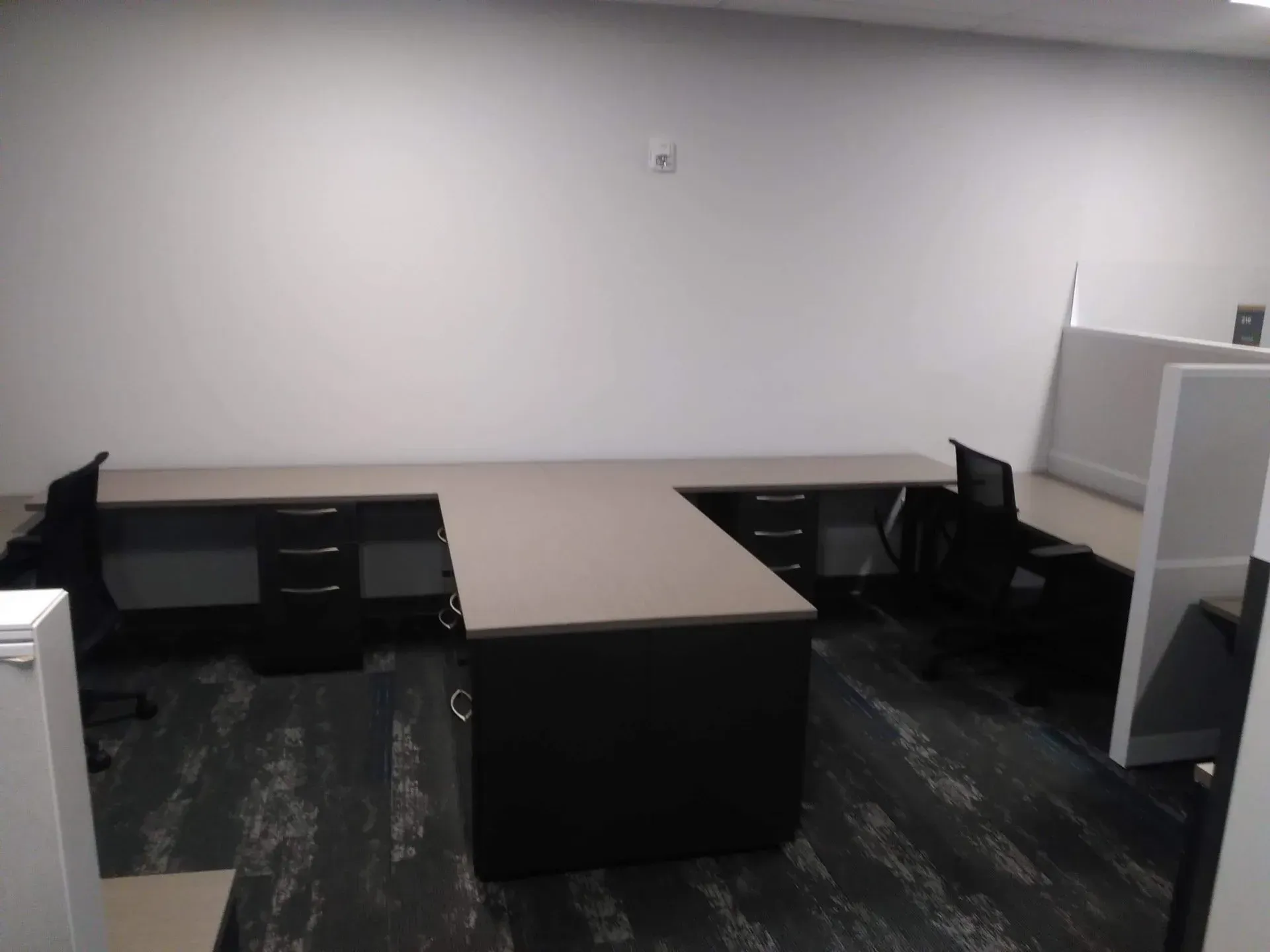 Empty office with L-shaped desks and cubicles under bright overhead lighting.