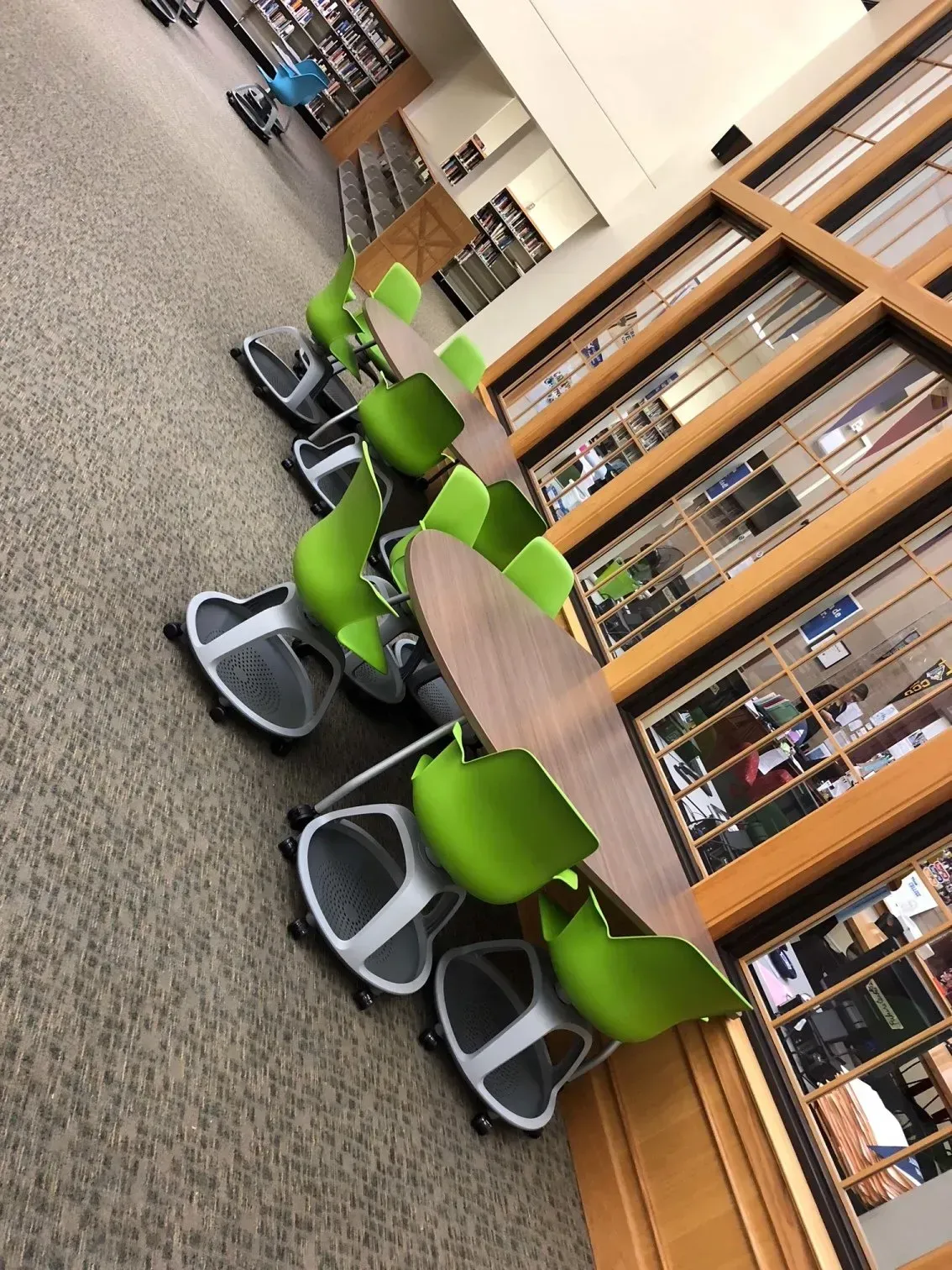 Quiet library study area with green chairs and wooden tables on a carpeted floor