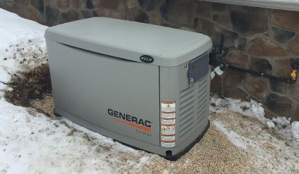 A generator is sitting in the snow next to a stone wall