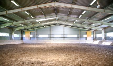 a large empty indoor riding arena with a dirt floor .