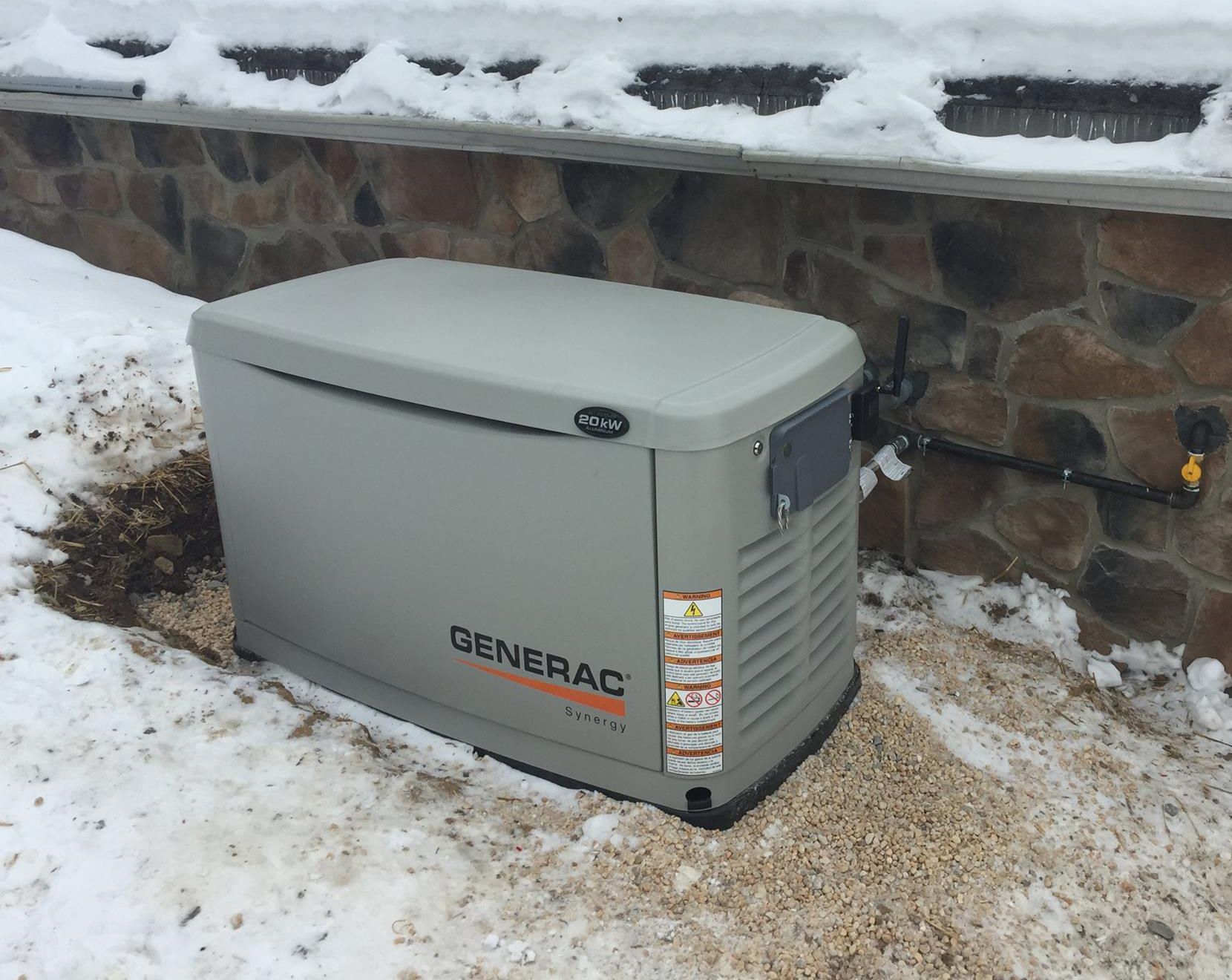 A generator is sitting in the snow next to a stone wall.