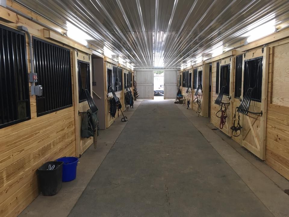 A long hallway filled with horse stalls and a blue bucket.