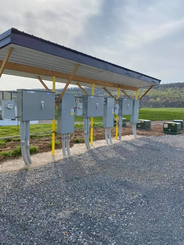 A row of electrical boxes under a roof in a gravel area.