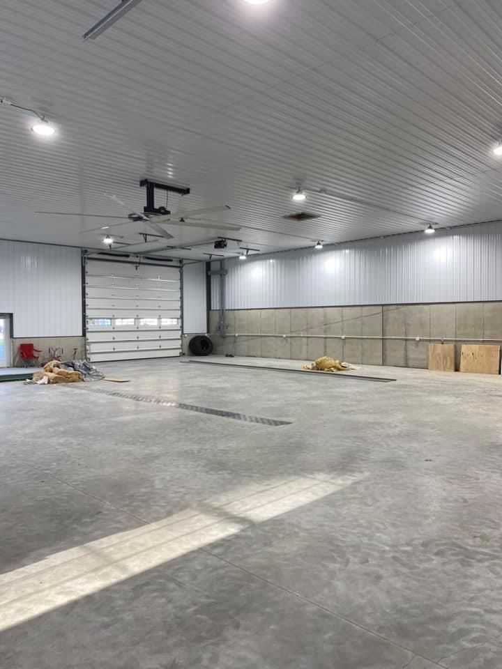 A large empty warehouse with a garage door and a ceiling fan.