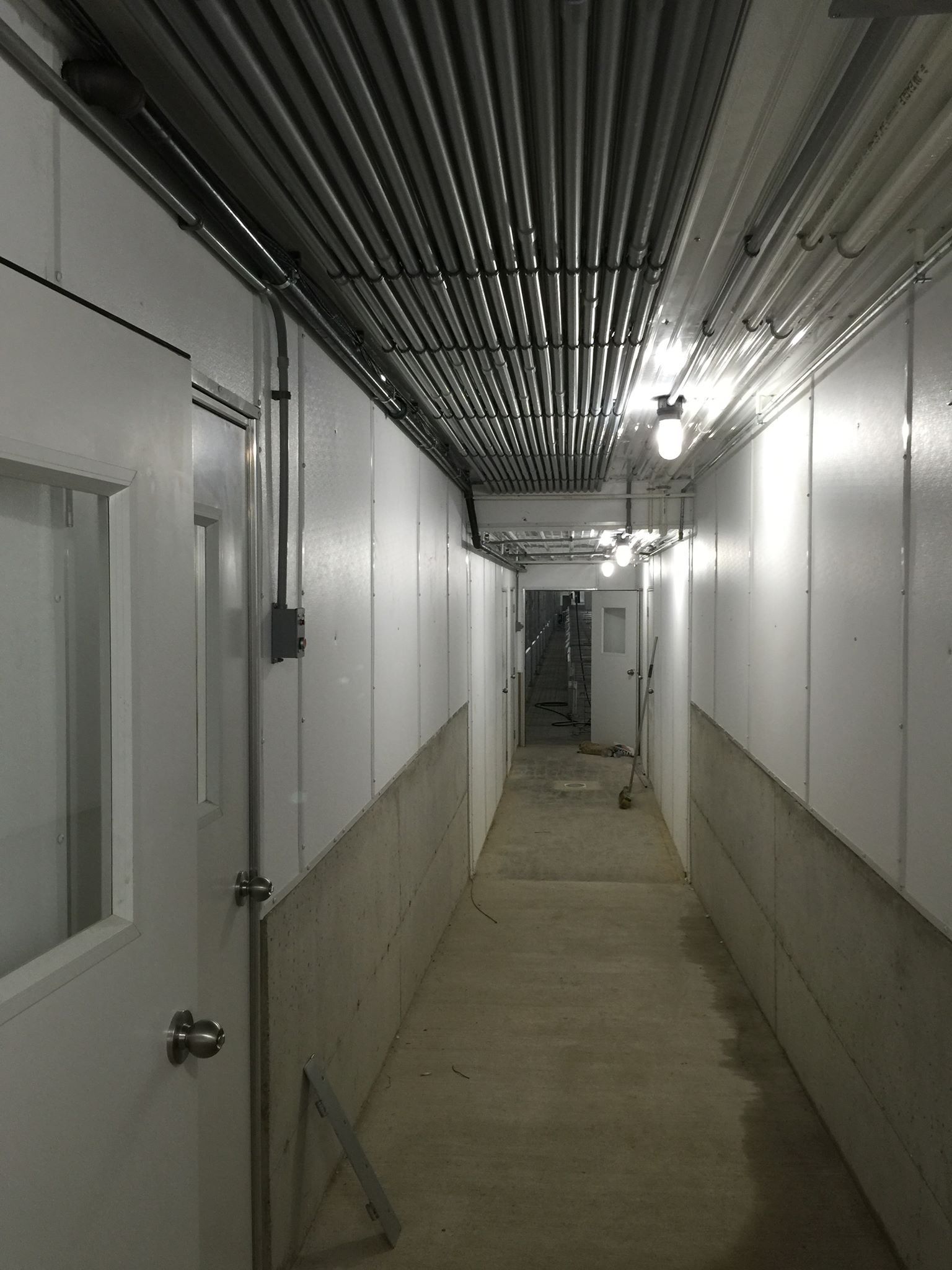 A long hallway with white walls and pipes on the ceiling.
