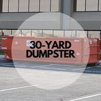 A 30 yard dumpster is parked in a parking lot in front of a building.