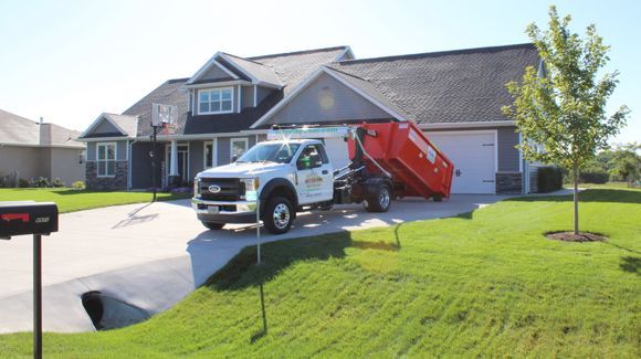 A dumpster truck is parked in front of a house.