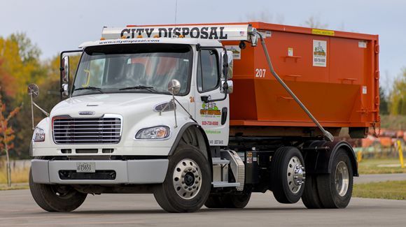 A city disposal dumpster truck is driving down a road.