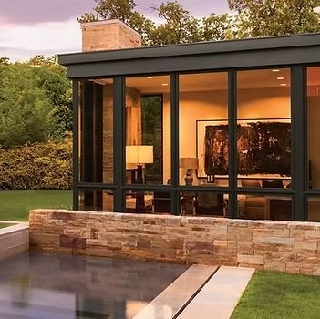 Modern home with large windows overlooking a rectangular pool and manicured lawn.