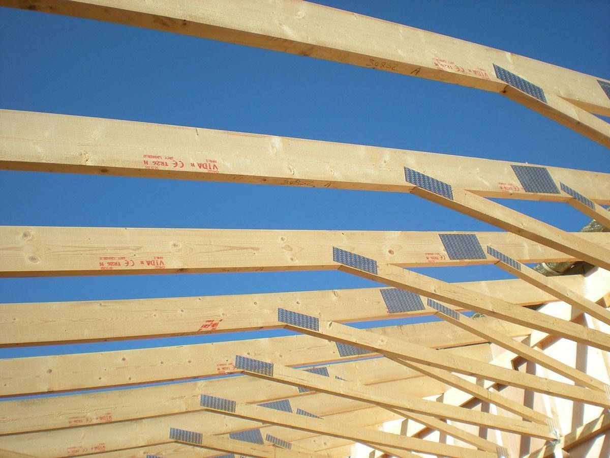 Wooden roof trusses with metal connectors against a blue sky.
