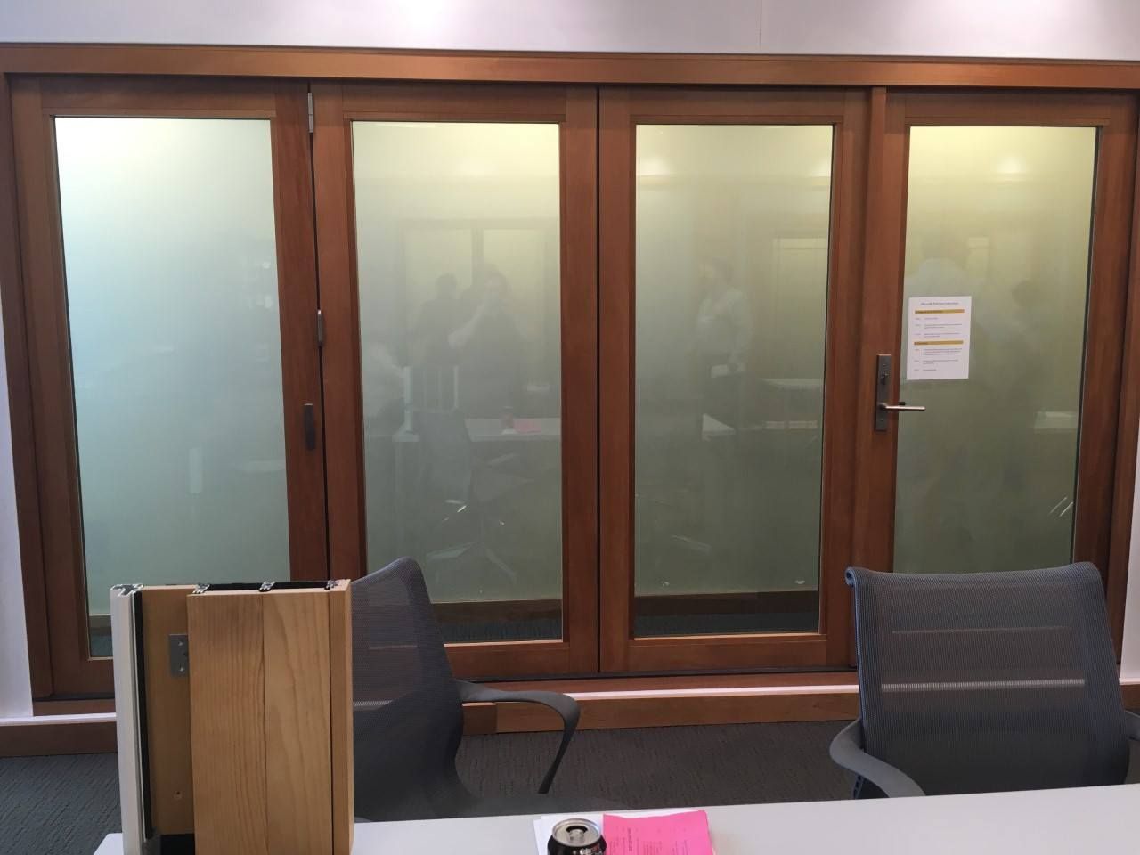 Wooden-framed glass doors partially frosted, revealing an office space with furniture and people inside.