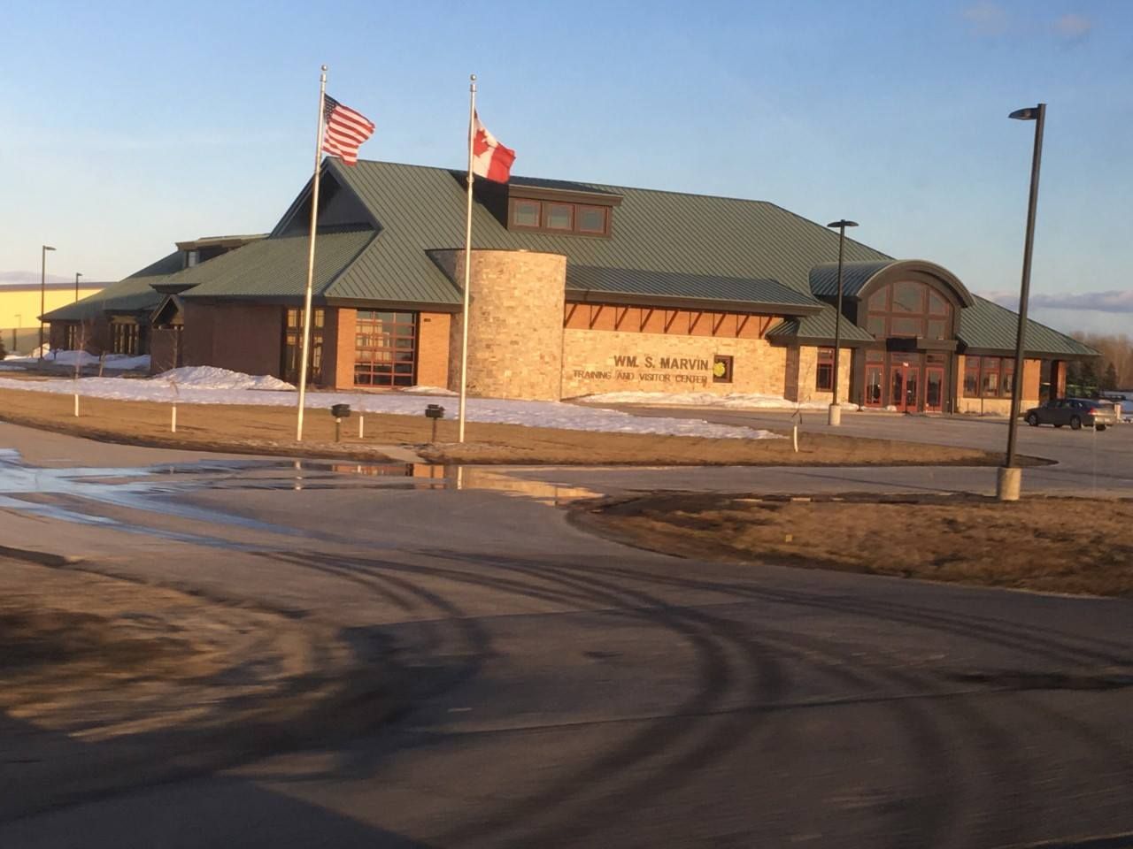 Building with brick and a green roof, flying US and Canadian flags.