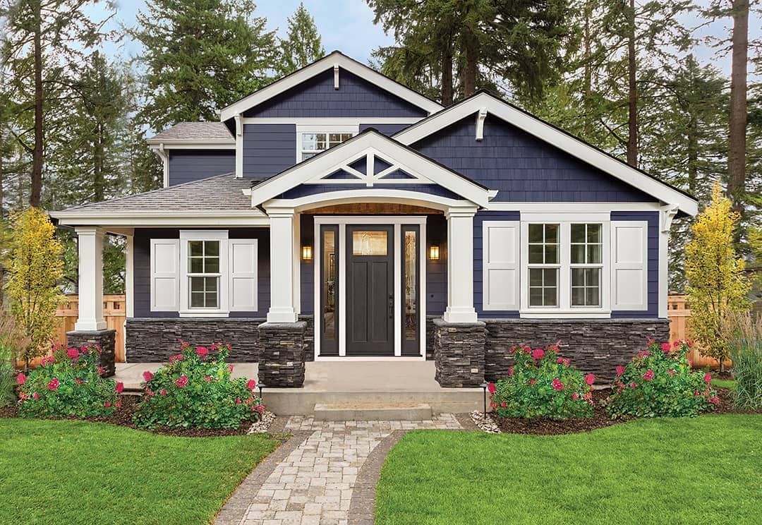 Blue house with white trim, porch, and stone accents; pathway leads to front door; surrounded by greenery.