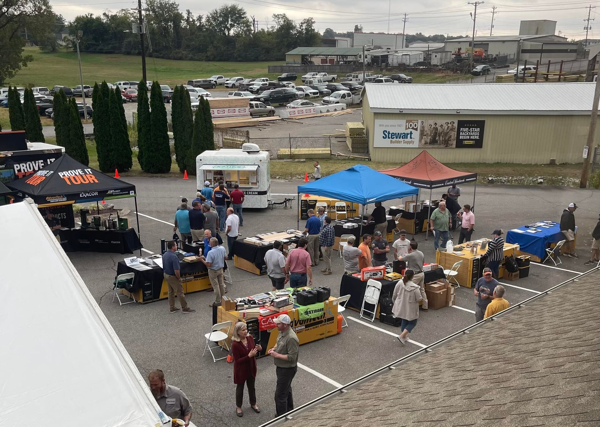 Outdoor food festival with vendors, people, tables, and food, in a parking lot.