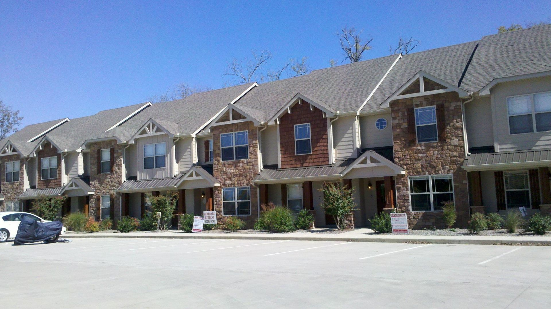 Row of townhouses with stone and brown accents, blue sky, parked car in front.