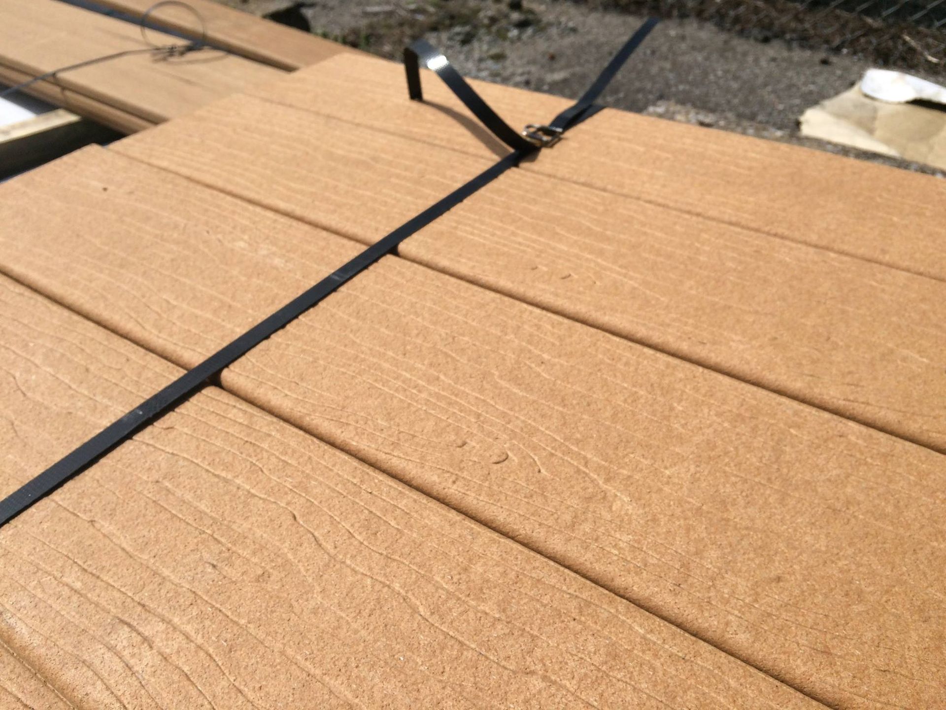 Bundle of light brown composite deck boards secured with a black strapping band.