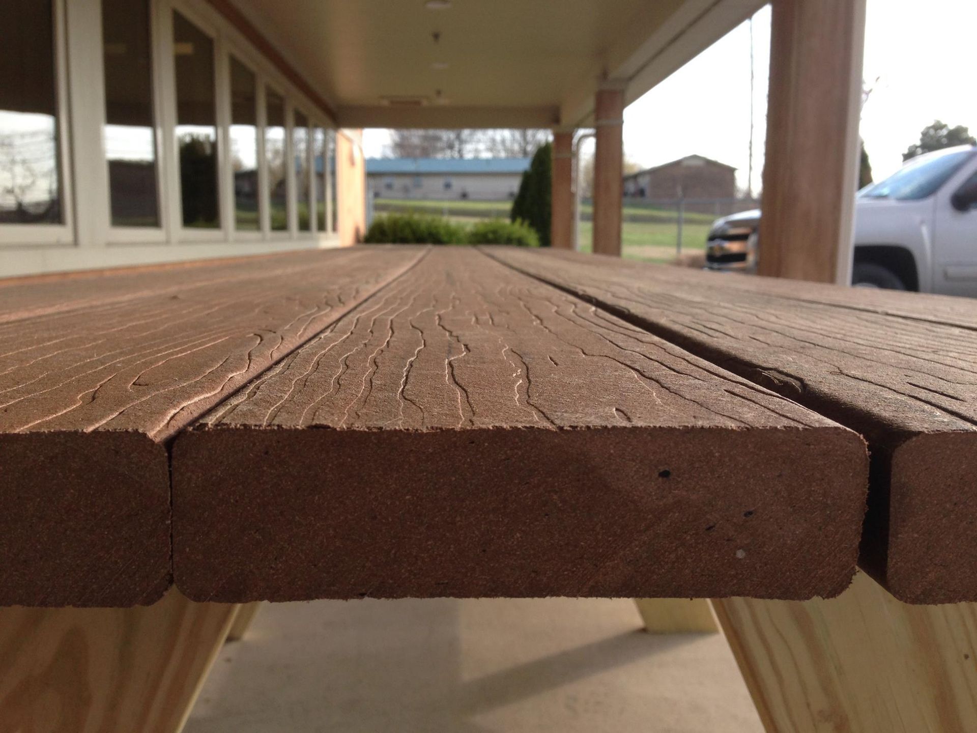 Brown composite picnic table with weathered texture, viewed close-up. Light brown wooden supports.