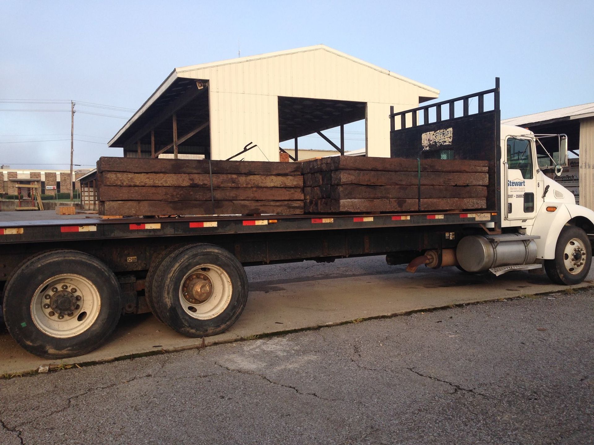 Flatbed truck loaded with wooden railroad ties parked near a white building.