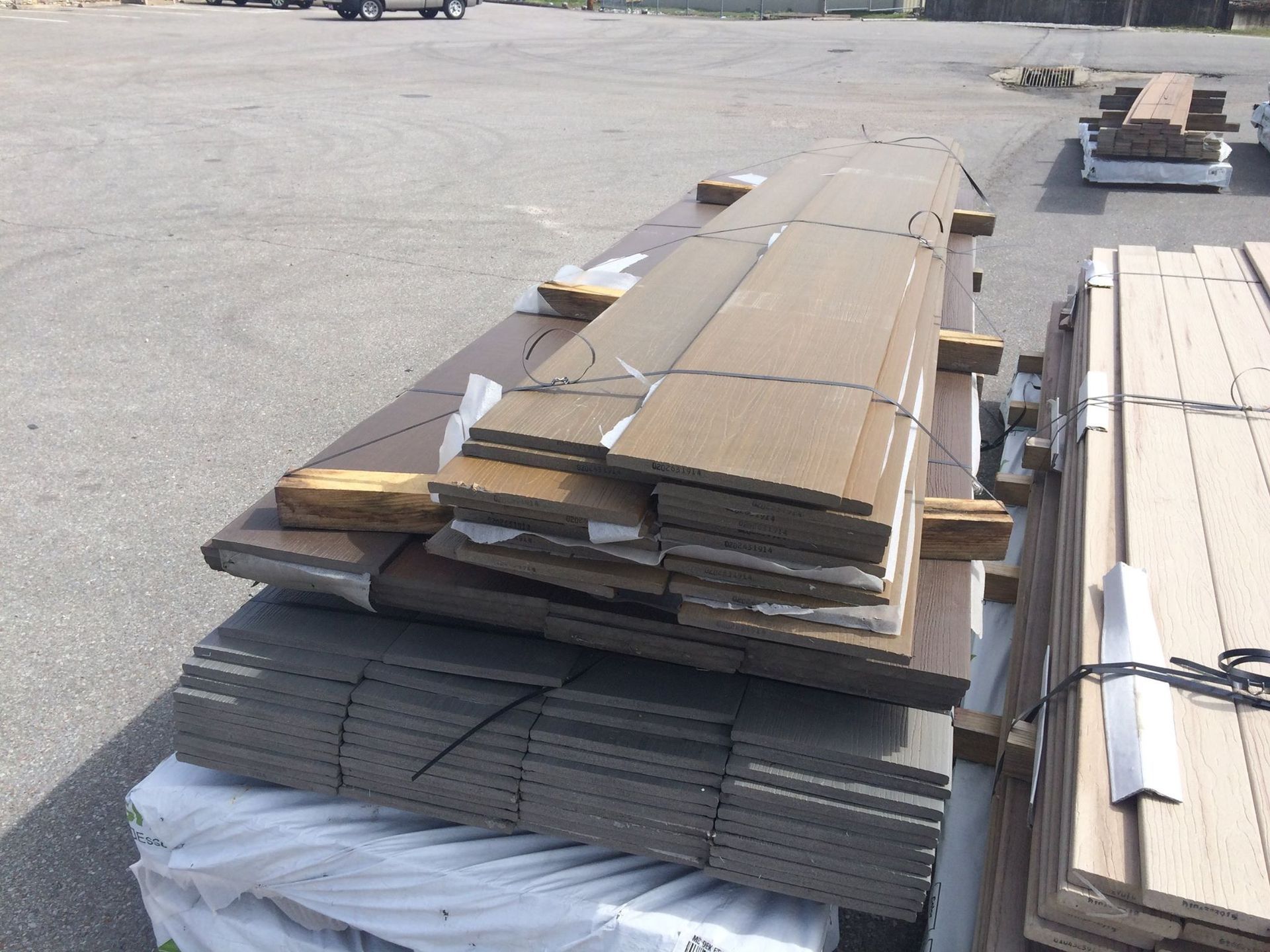 Bundles of brown and gray planks, stacked on pallets, outdoors.