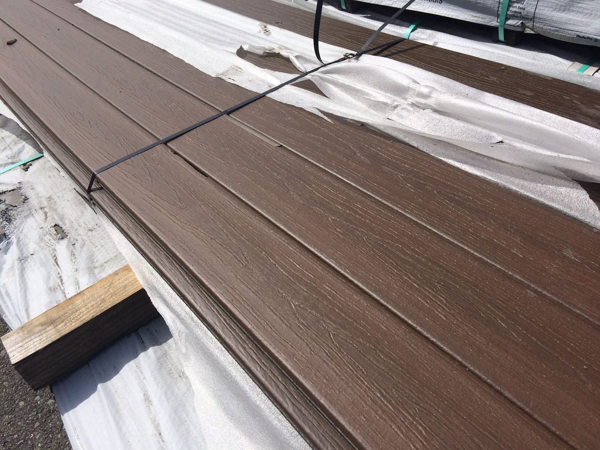 Brown composite deck boards stacked and bound with black straps.