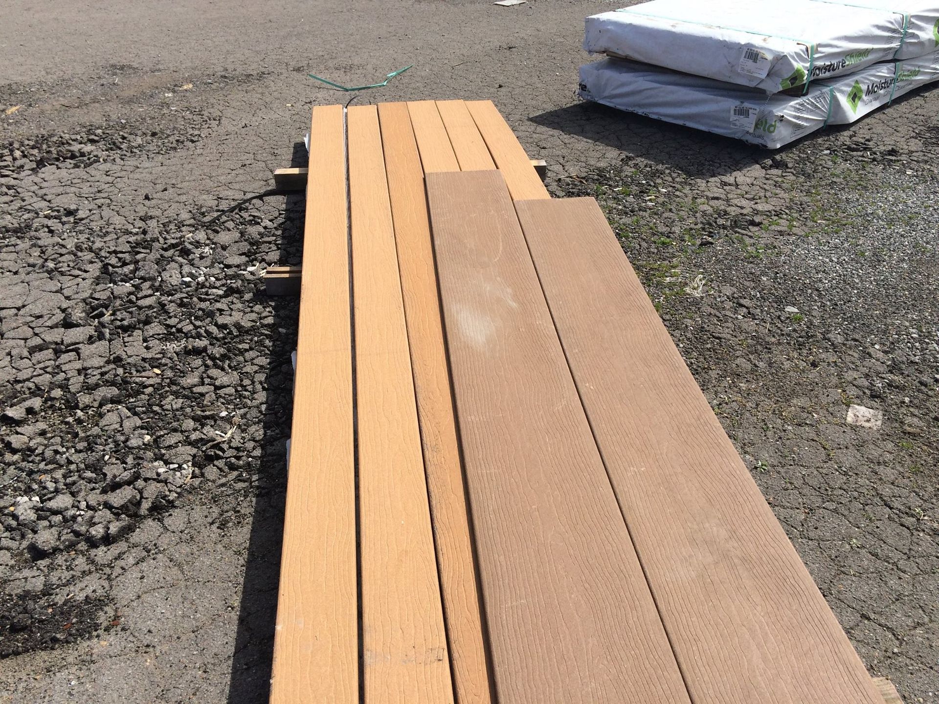 Several long wooden planks, various shades of brown, rest outdoors on a gravel surface.