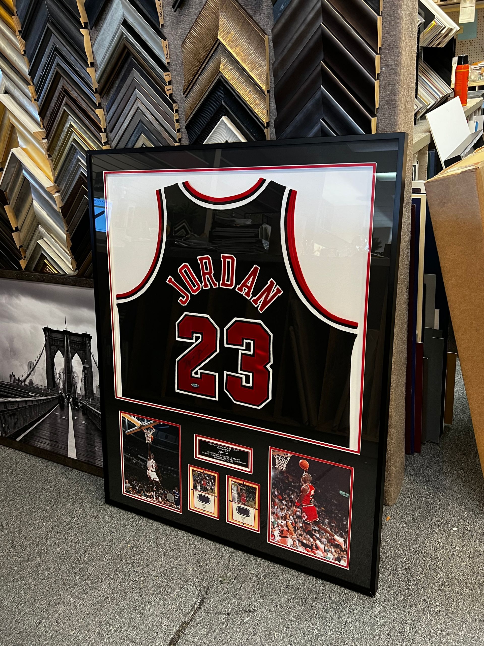 A framed Chicago Bulls Michael Jordan jersey with photos and a plaque, displayed in a framing shop.