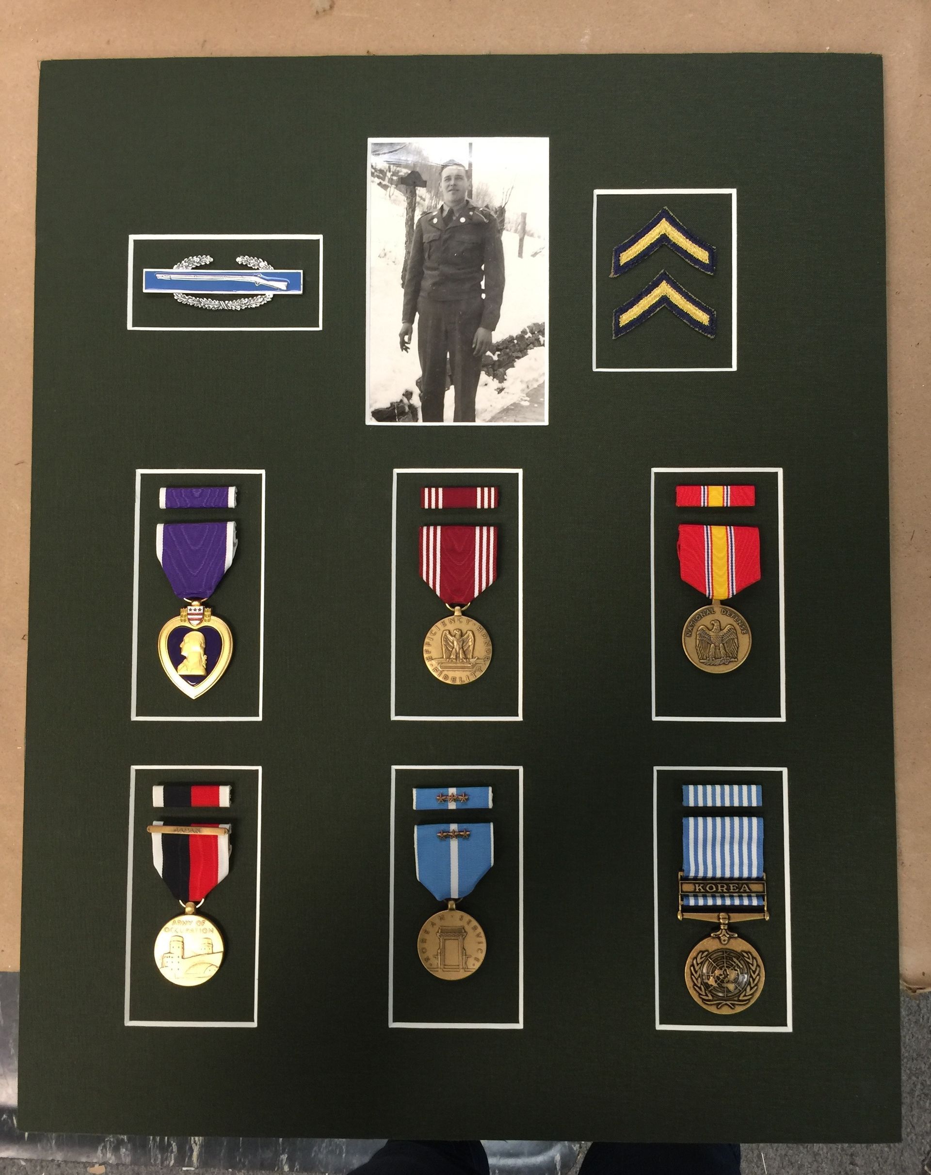A display featuring a soldier's photo, military medals, and chevron rank insignia on a green background.