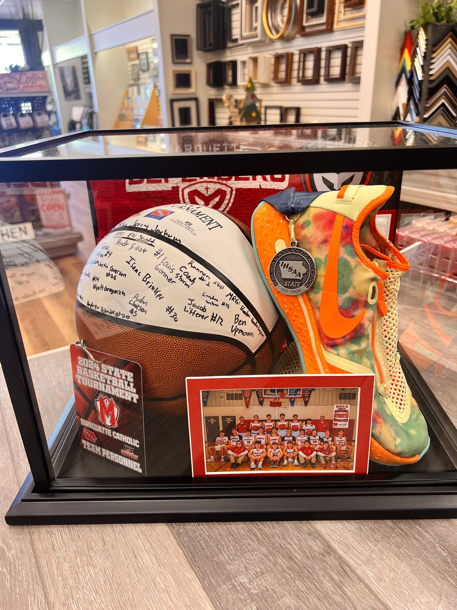 A display case holds a signed basketball, an orange and floral patterned sneaker, and a framed team photo.