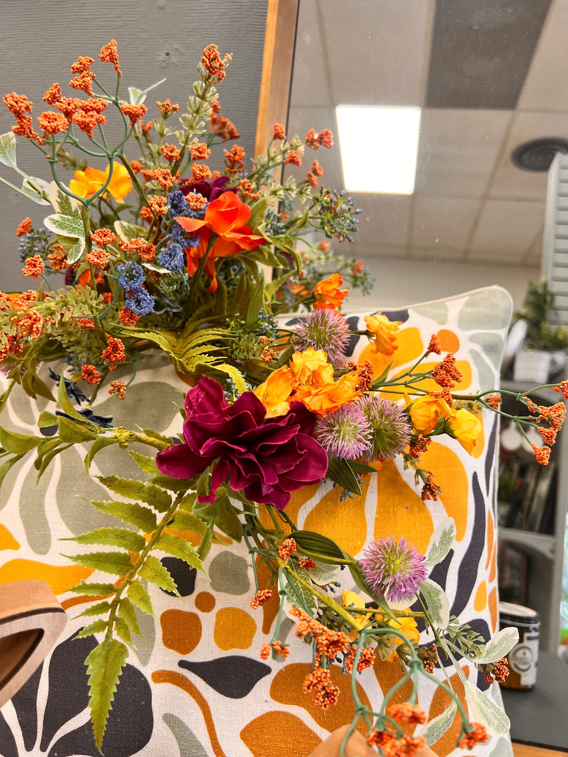 A decorative floral arrangement with orange, purple, and yellow flowers rests on a pillow with a yellow abstract pattern.