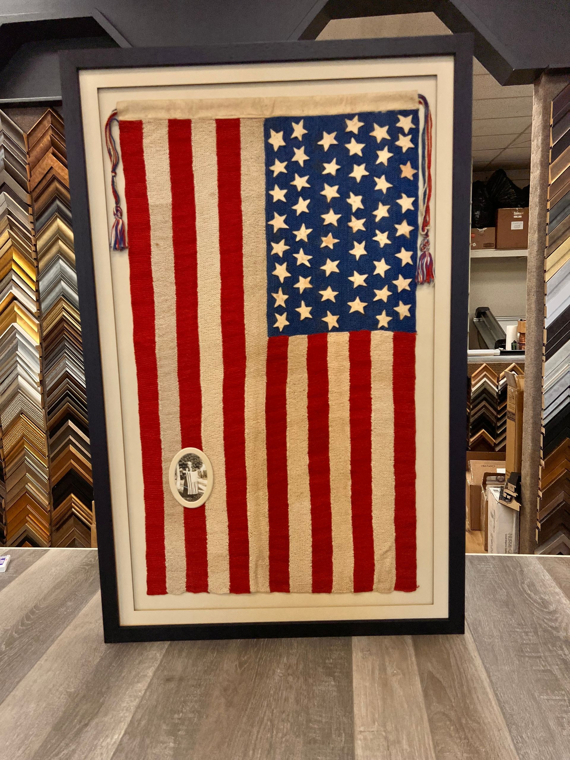 A framed vintage American flag with a small photo pinned to it, set against a background of various picture frame samples.
