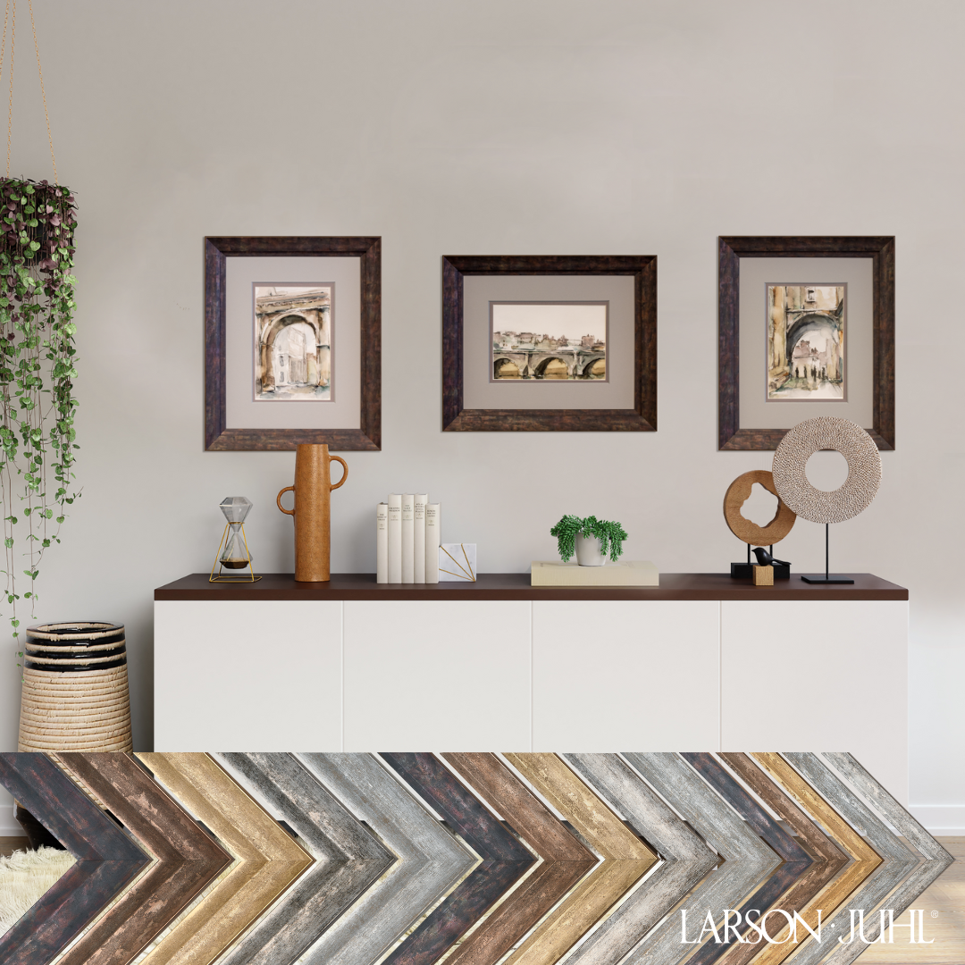 Three framed art prints hanging above a white console table with home decor, and a display of wood frame samples below.