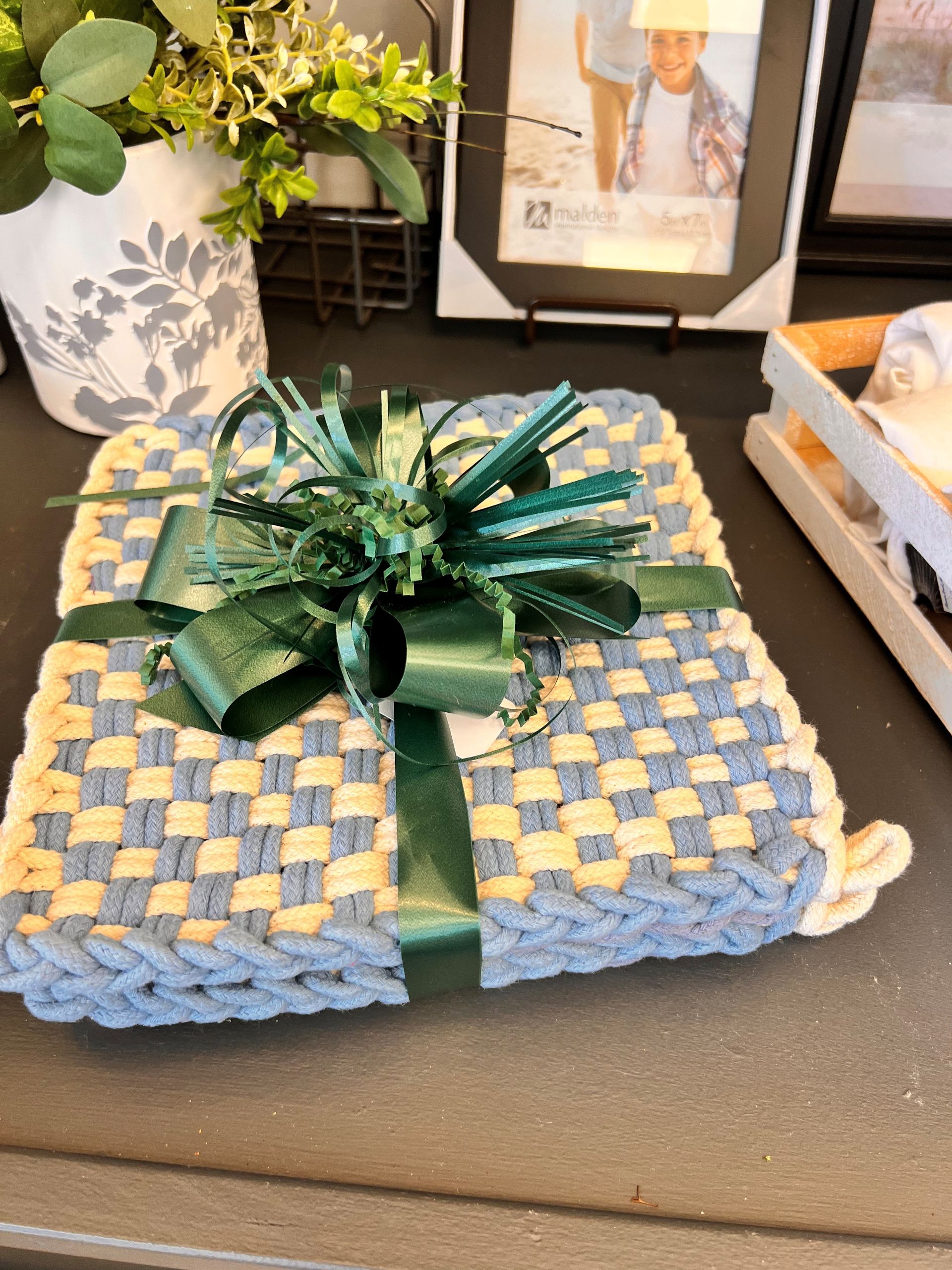 Wrapped blue-and-green gift on a table with a decorative bow, beside a plant and framed photo.
