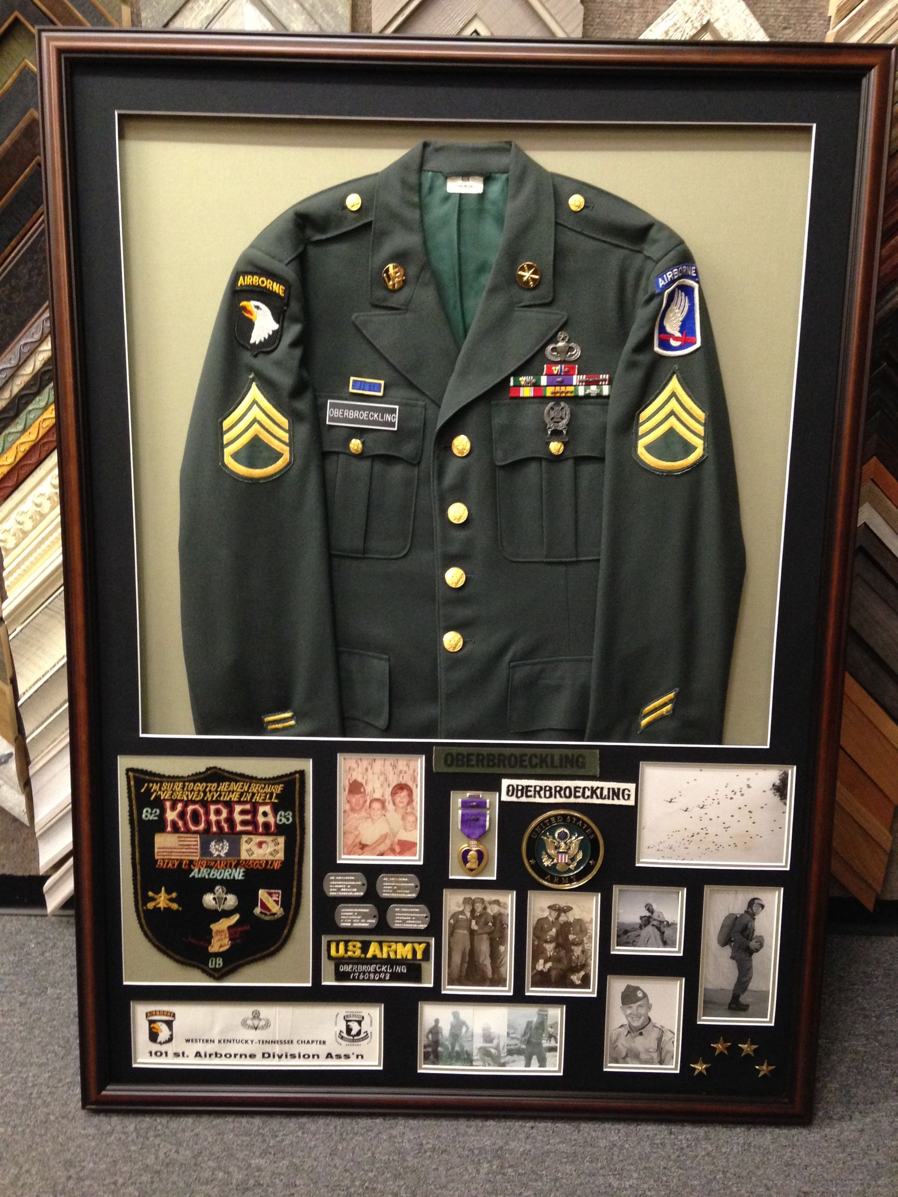A framed US Army uniform with patches, medals, and vintage photographs displayed below in a memorial shadow box.