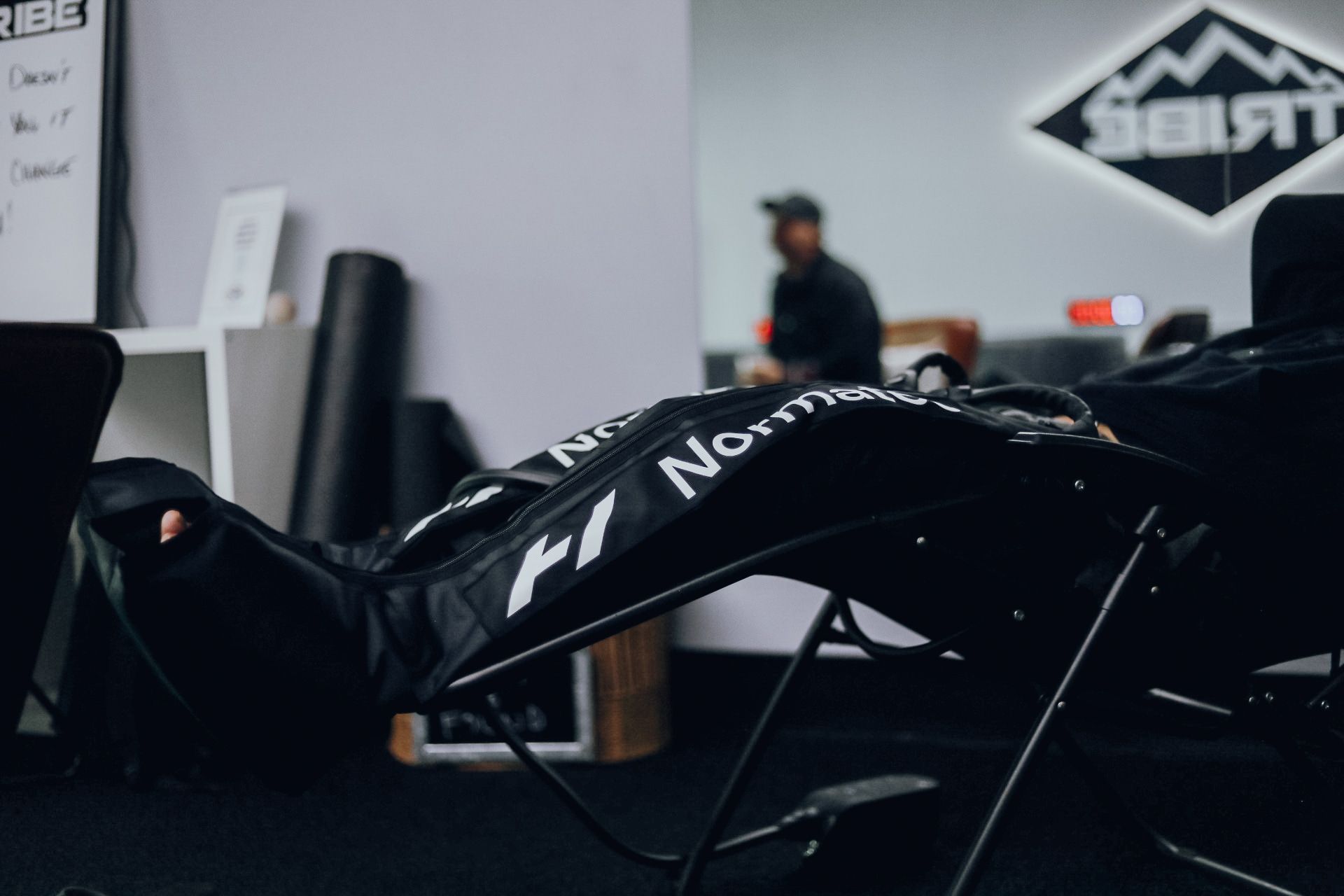 Man reclines in a chair indoors, wearing a black outfit with "Normal" and F1 logo.