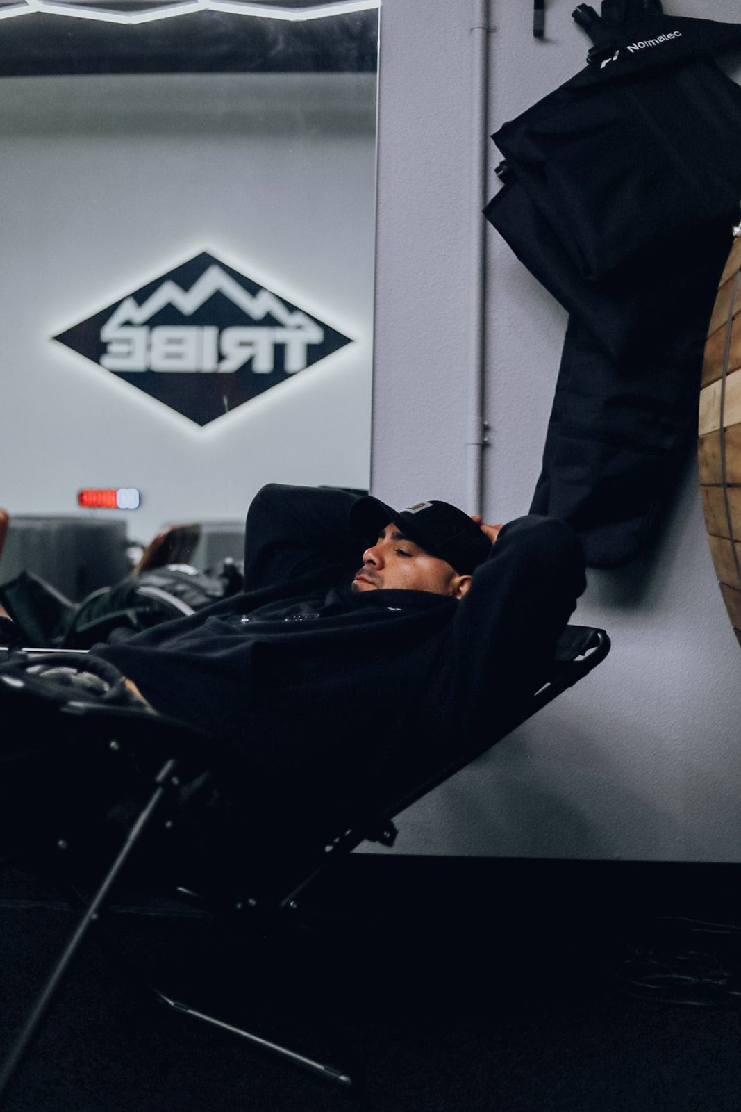Man resting in a black chair at the gym, eyes closed, logo 