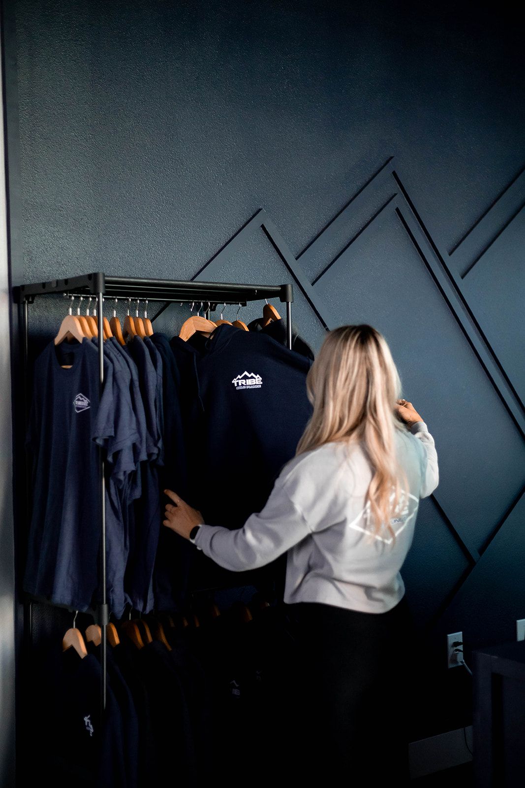 Woman browsing dark blue clothing on a rack in a shop with a mountain-themed wall design.