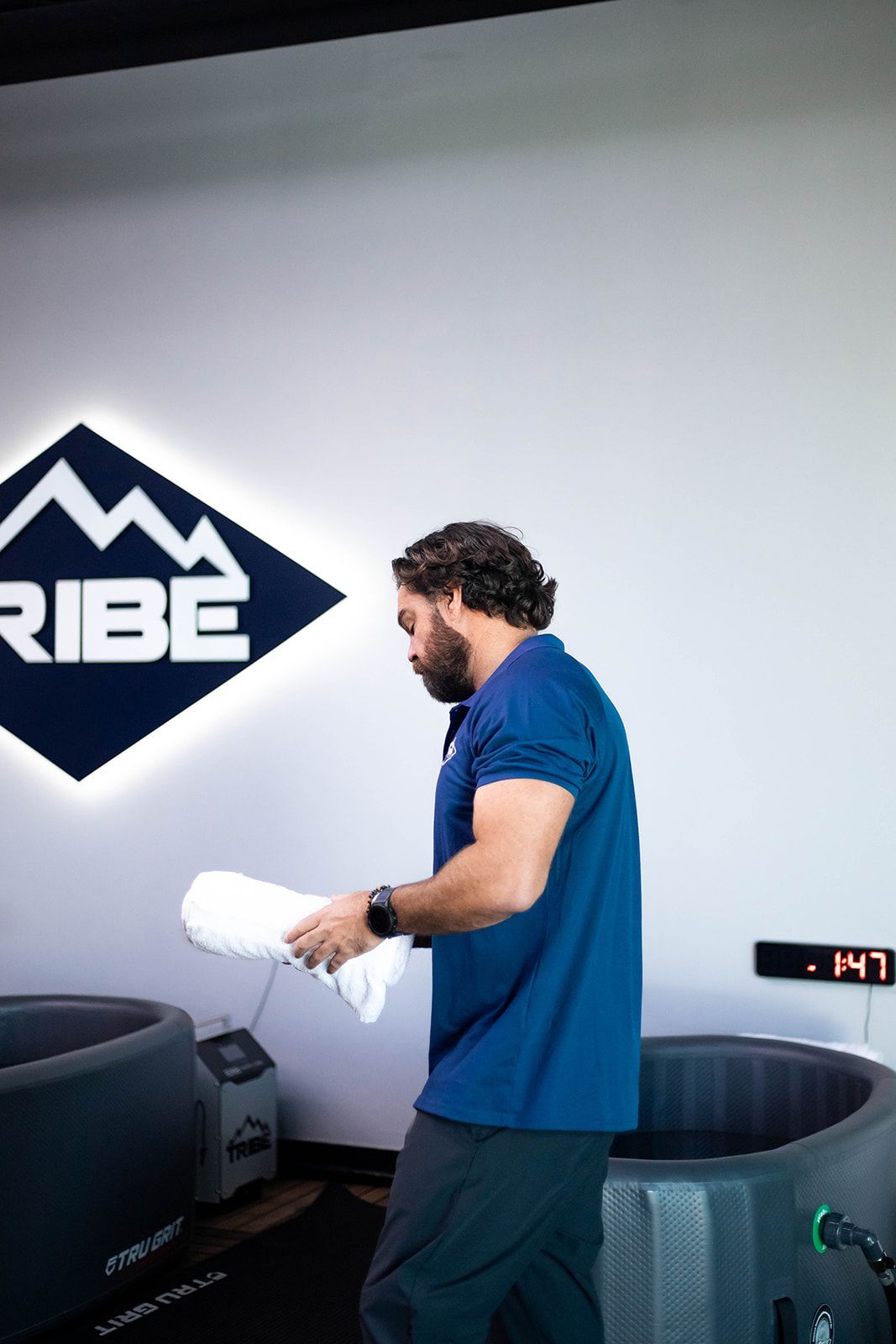 Man with towel near cold plunge tubs in a fitness center. White and dark blue colors are visible.