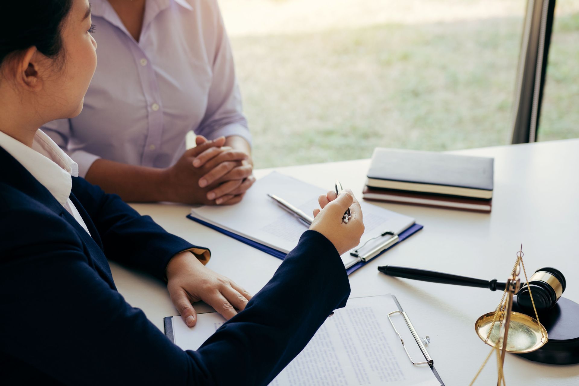 A lawyer in a dark suit reviewing documents with a client at a desk, with a gavel and scales of justice visible.