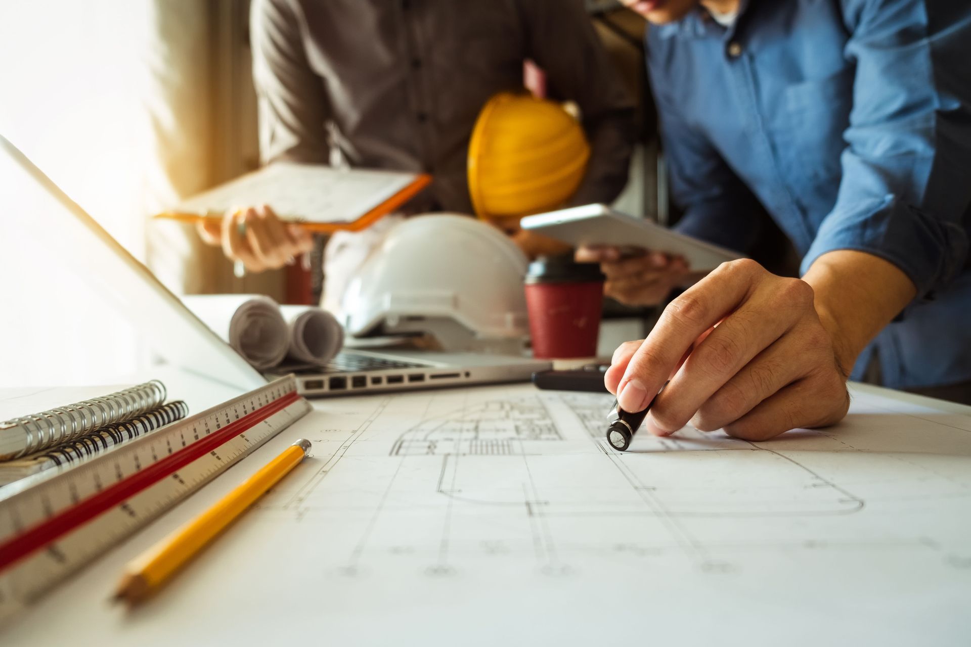 Architects reviewing blueprints with laptop, hard hats, and tools on desk.