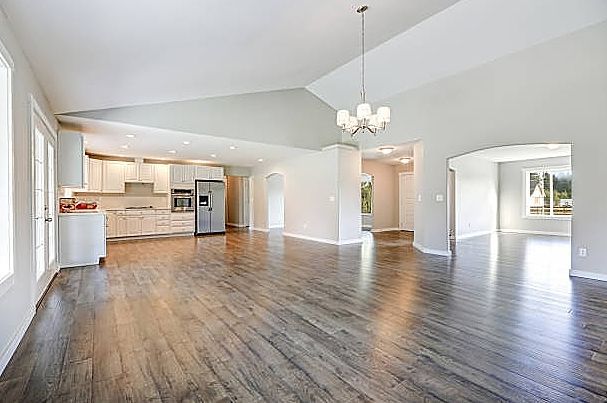 A large empty living room with hardwood floors and a kitchen.